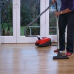 starija žena usisava parket sa crvenim usisivačem