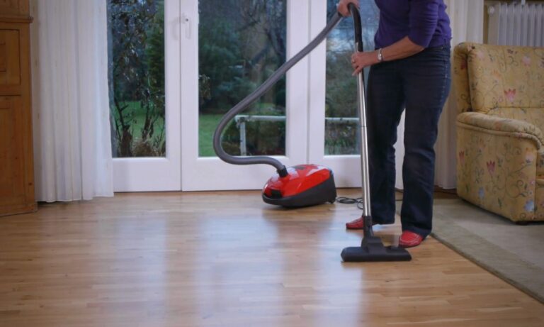 starija žena usisava parket sa crvenim usisivačem